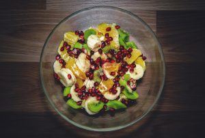 sliced bananas in a fruit salad with kiwi, oranges, and pomegranates