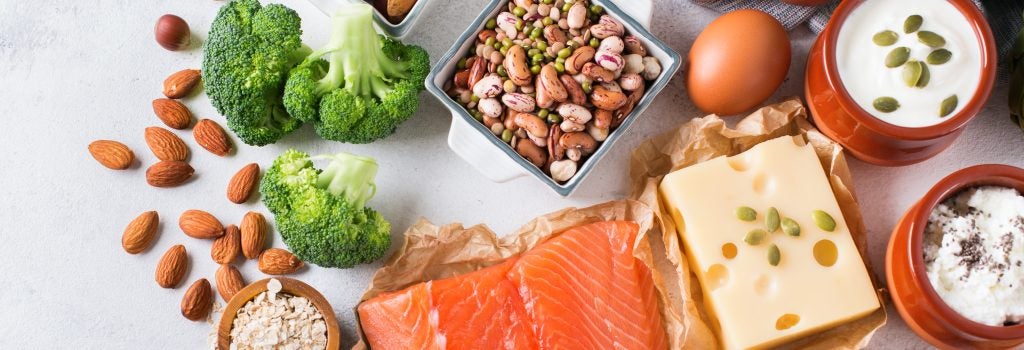 A variety of protein foods, including egg, salmon, beef, chicken, beans, lentils, almonds, quinoa, oats, broccoli, artichokes, yogurt, cheese, and tofu