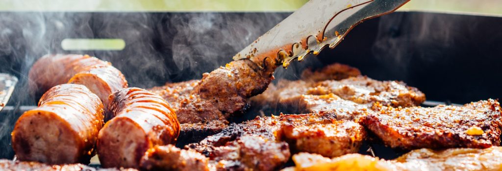 grill with meats including hot dogs, steak, and pork