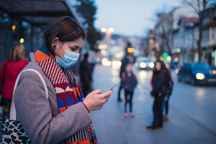 Woman looking at a cell phone with a face mask on in a city street