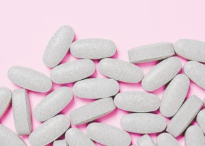 grey multivitamin tablets on a pink surface