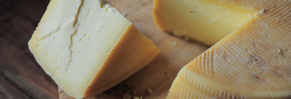 Wedge of cheese cut from a larger wheel; sitting on top of a wooden cutting board