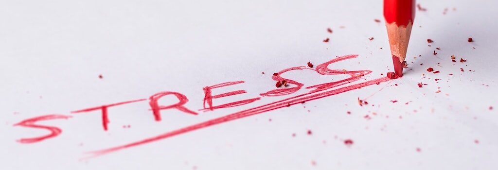 the word stress written out in a red colored pencil, with pressure being applied to the pencil causing the tip to break