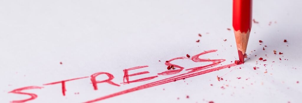 the word stress written out in a red colored pencil, with pressure being applied to the pencil causing the tip to break