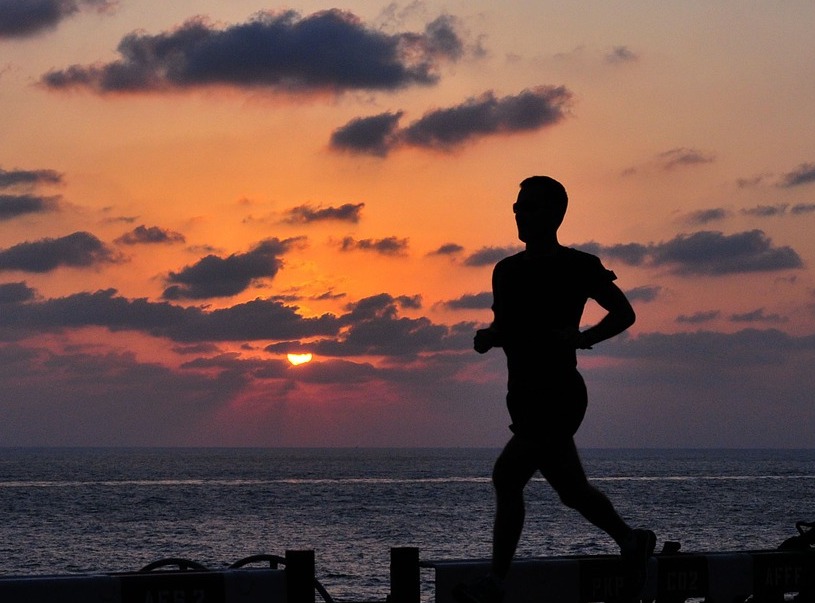 silhouette of man running at dusk amidst background of setting sun in clouds and ocean
