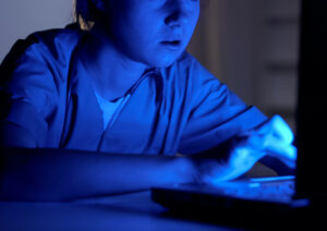 nigh shift nurse sitting at a computer emitting blue screen in the dark