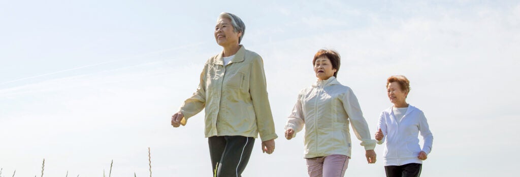 three women, older in age, walking up a grassy hill with blue sky behind them