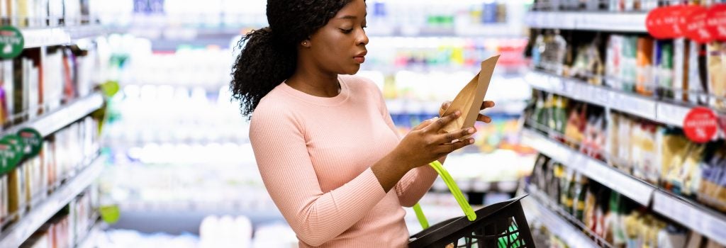 A women grocery shopping and looking at the label on a package of food in her hand
