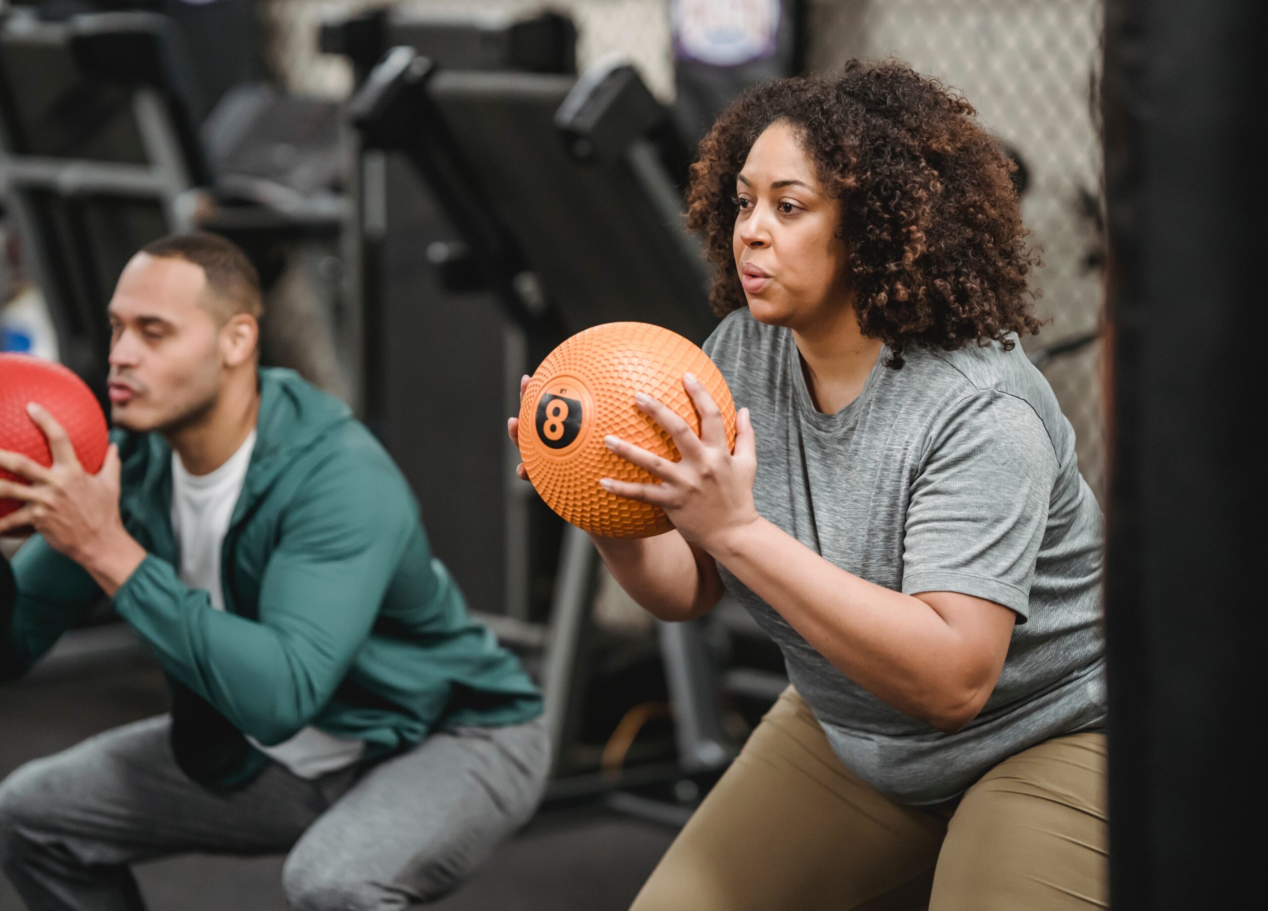 two people doing squats in a gym with a medicine ball