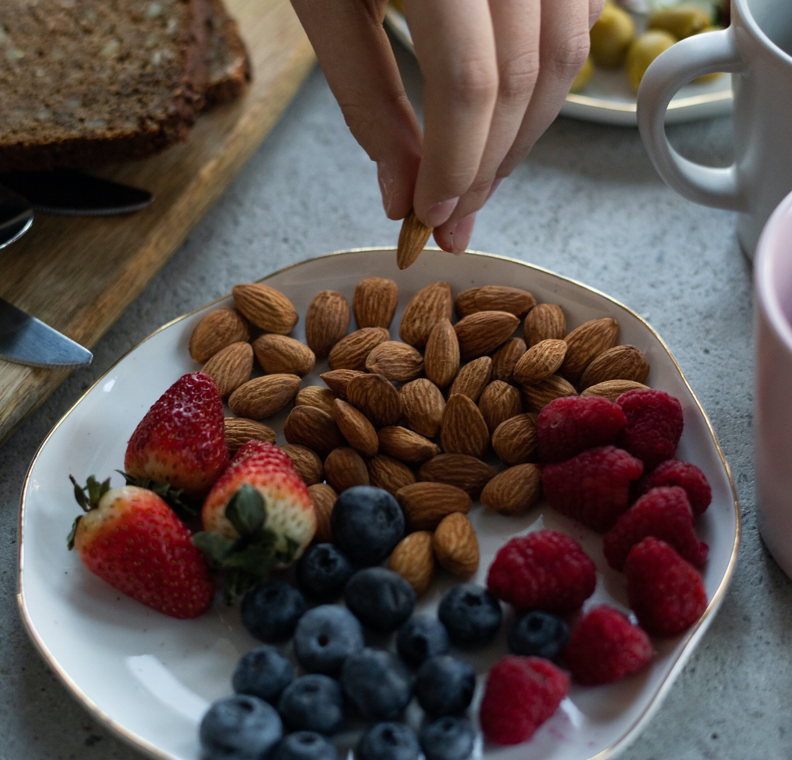 a person picking up an almond from a plate with nuts and berries