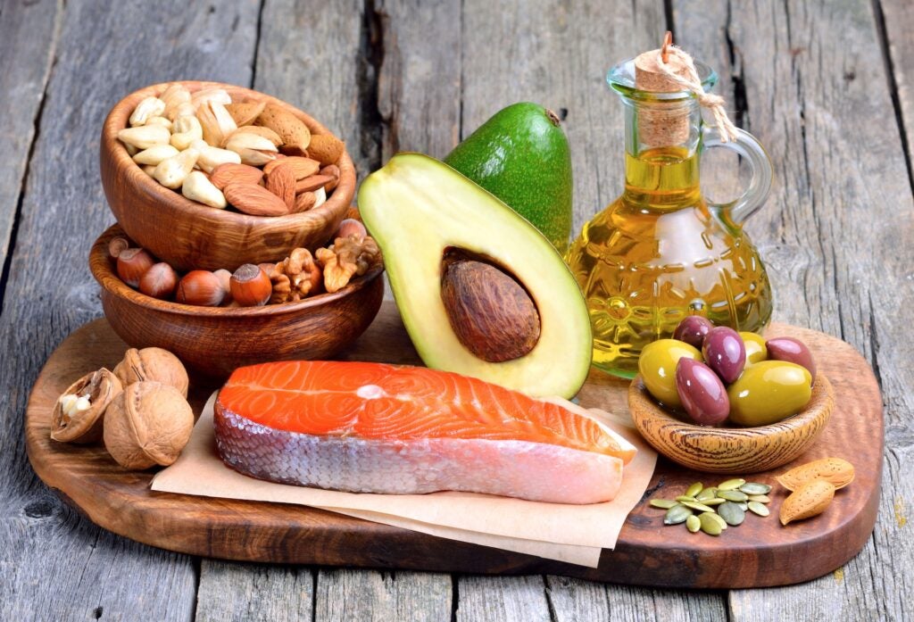 wood board with selection of healthy fats, including olive oil, avocado, salmons and nuts