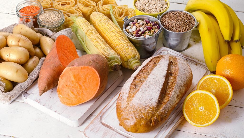 Carb containing foods on table (bread, potatoes, corn, pasta, fruits, grains, nuts)