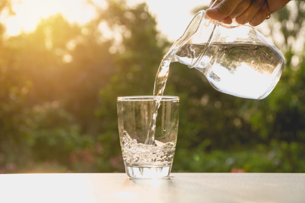 person pouring water from pitcher into glass on table with sun in background