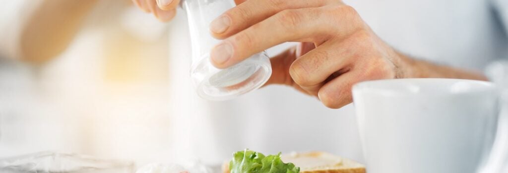 close up of man's hands seasoning plate of food with salt shaker