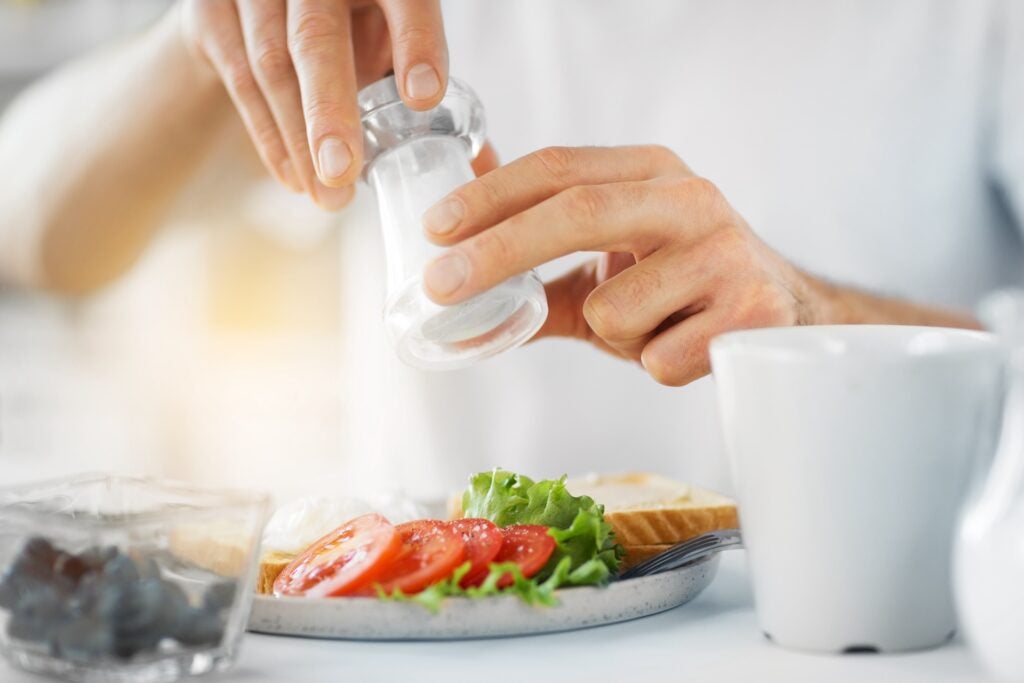 close up of man's hands seasoning plate of food with salt shaker