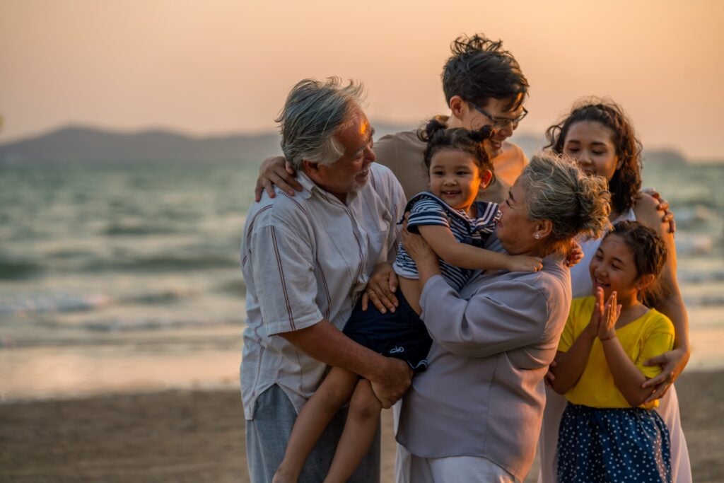 three generations of a family hugging on a beach