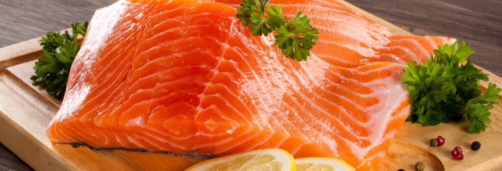 two fresh salmon fillets on a wooden cutting board with lemon and herbs