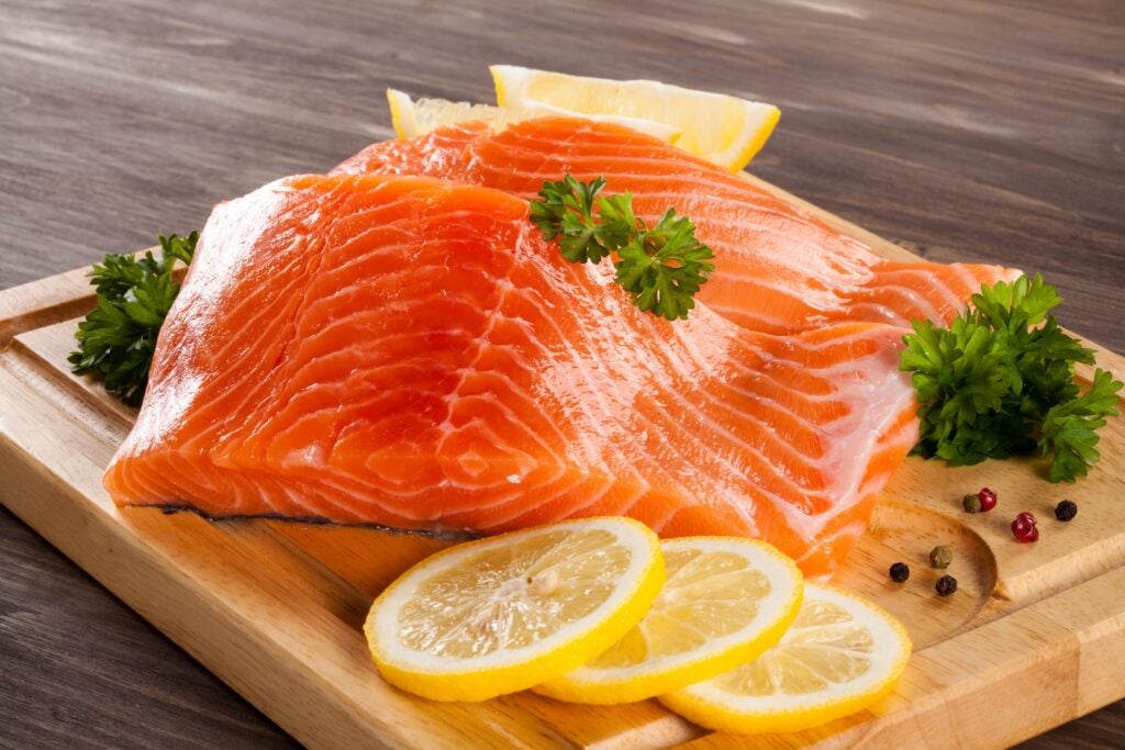 two fresh salmon fillets on a wooden cutting board with lemon and herbs