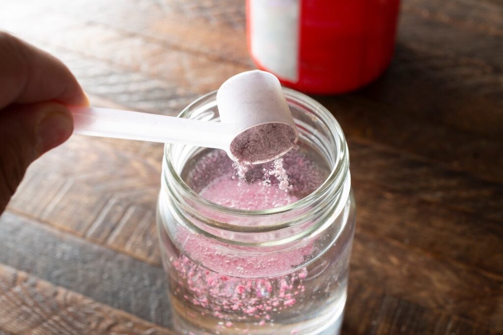A view of a hand scooping electrolyte powder into a glass of water.